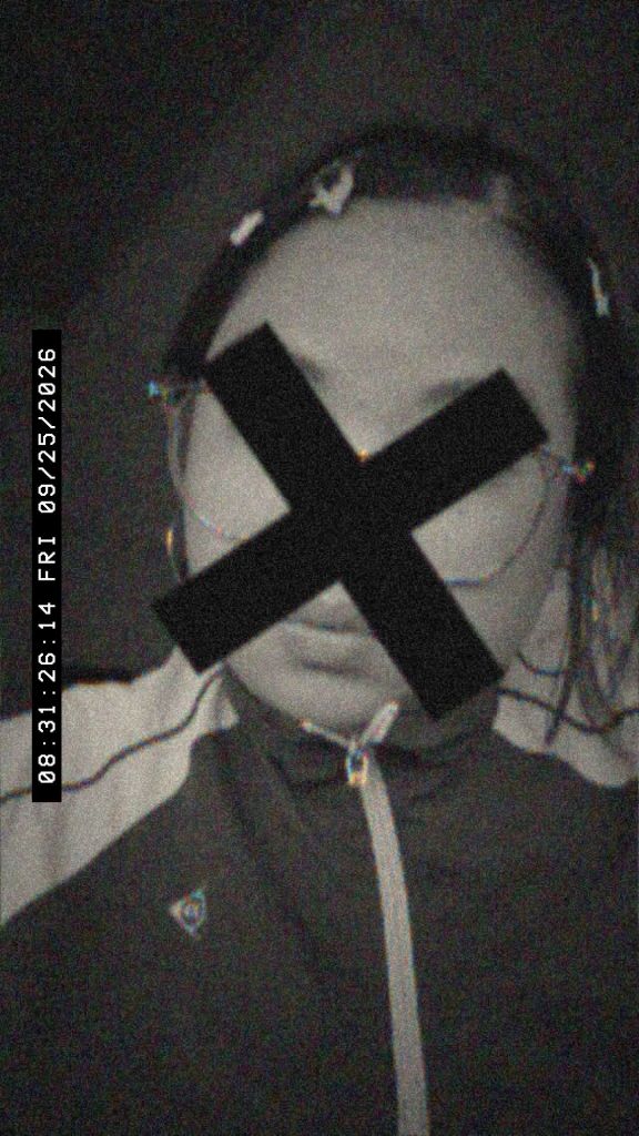 A person wearing a zip-up jacket with visible stripes and hair accessories, their face obscured by a black 'X' mark, captured in low light.